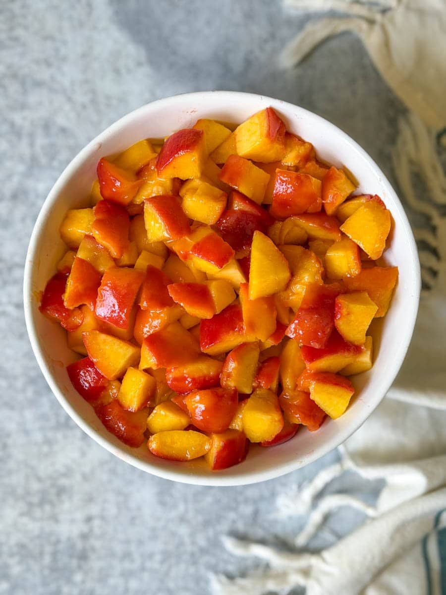 Chopped peaches fill a large white ceramic bowl. 
