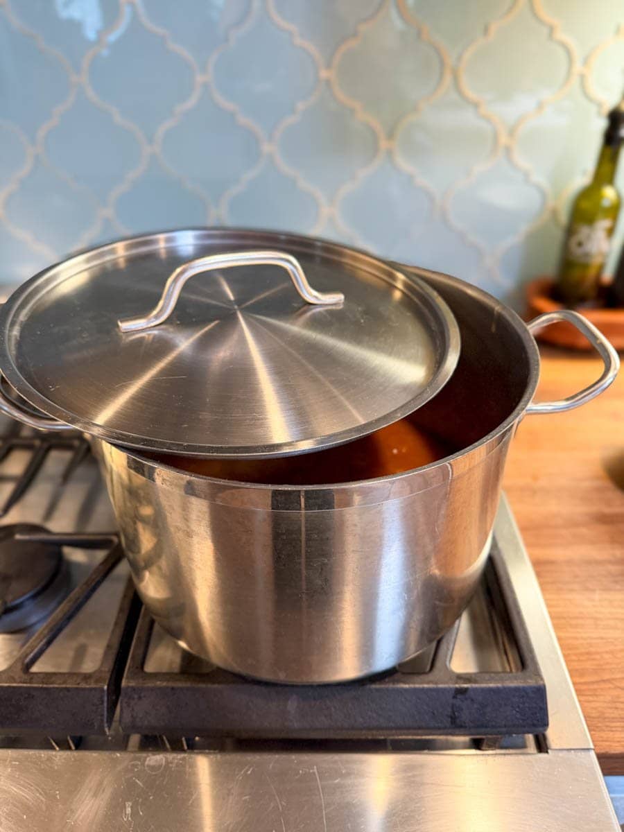 A large stock pot is on the stove with a lid partially covering the top of the pot. 