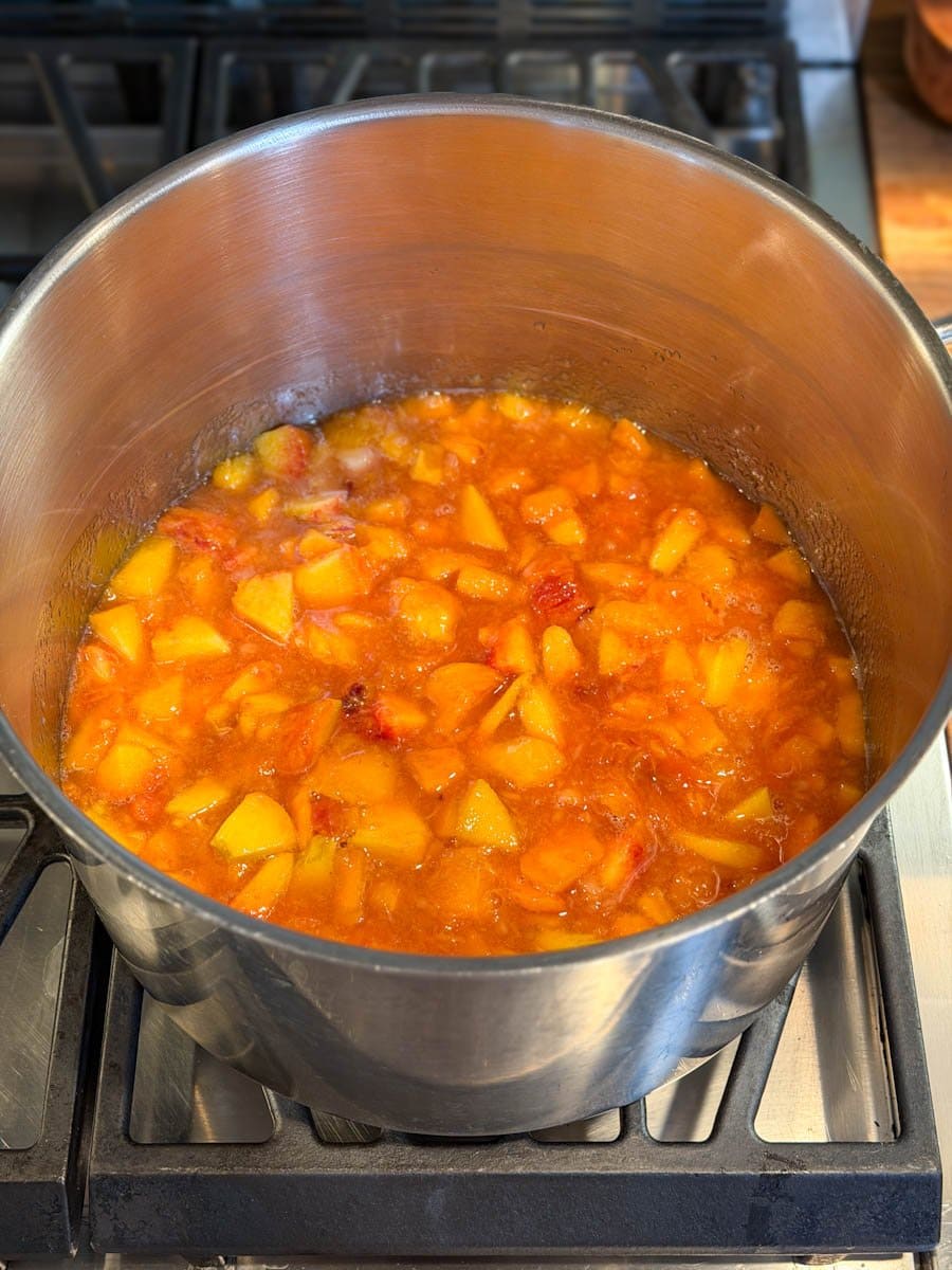 A stock pot partially full of chopped peaches simmers on the stovetop. 