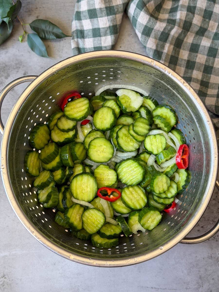 Cucumber mixture with peppers and onions are in a stainless steel colander after being thoroughly rinsed with water.