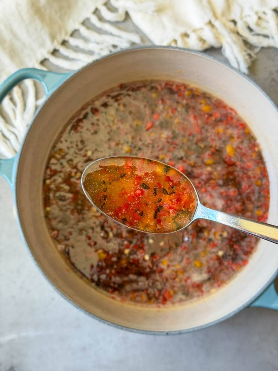 A spoonful of chili jam is held above a large pot of the jam.