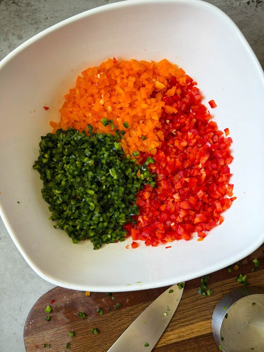 Chopped red, yellow, and jalapeño chilis are inside of a large ceramic bowl.