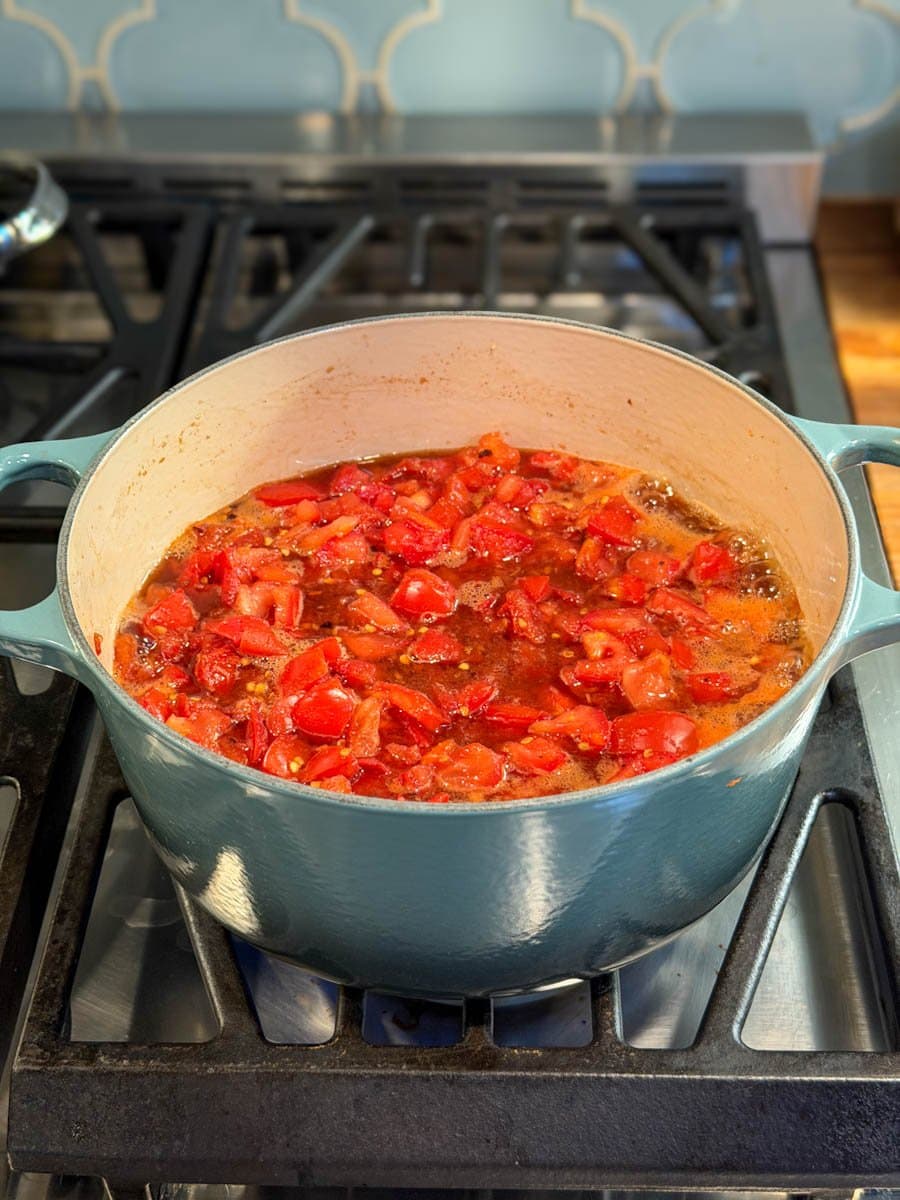 A large cooking pot is full of chopped tomatoes among other ingredients. 