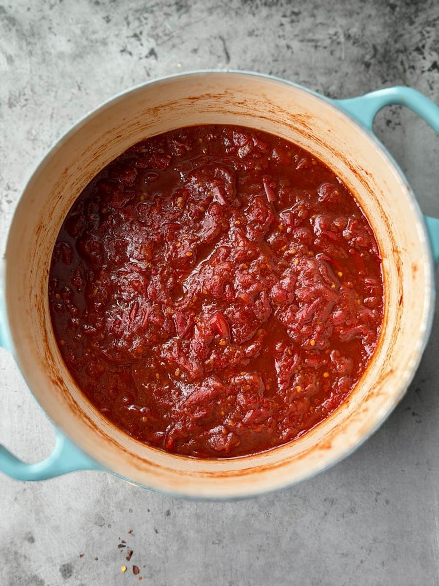 A heavy bottom cooking pot full of tomato jam that has been cooked and reduced down into a thick consistency. 