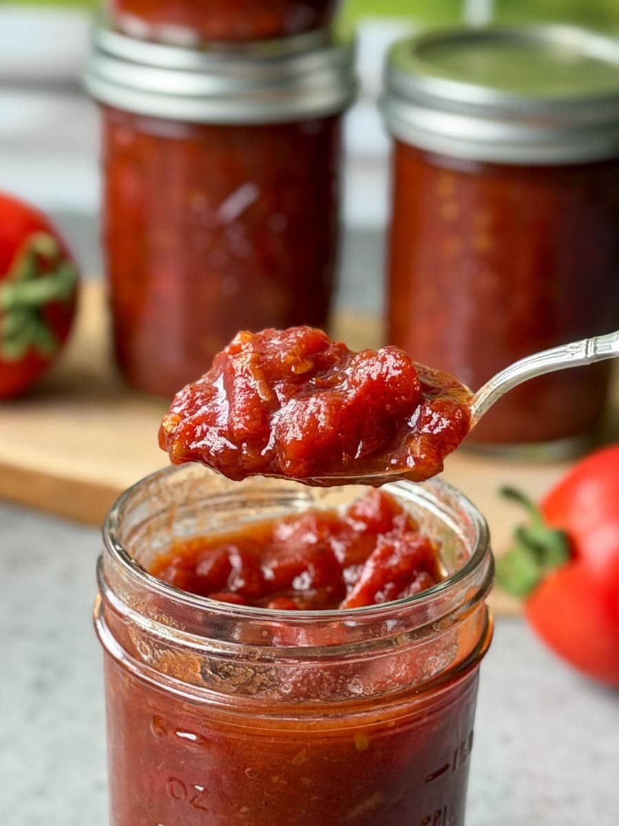 A half pint of preserves with a spoon held above the jar with a spoonful of the preserves. 