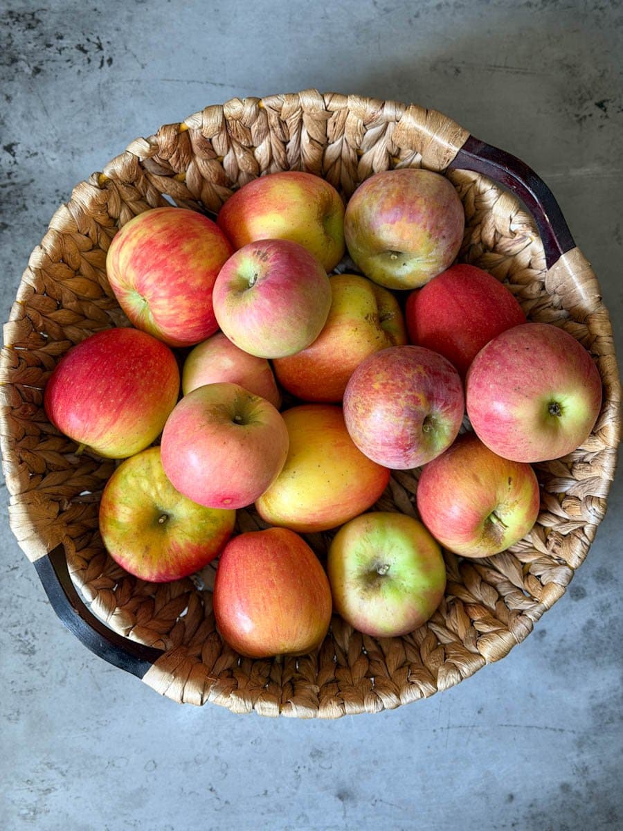 A round wicker basket of fresh apples of varying sizes and colors.