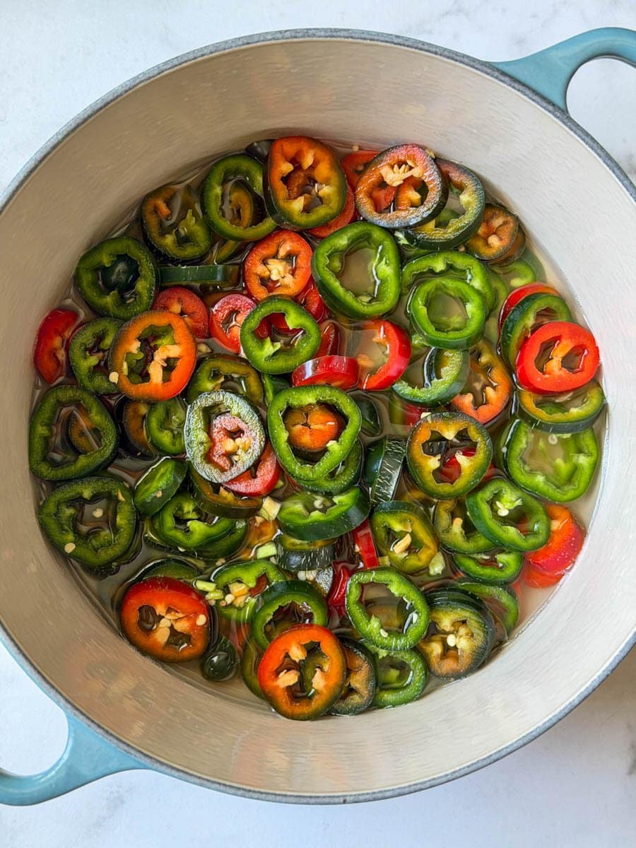 A stock pot is full of sliced pickled jalapeños floating in a brine.