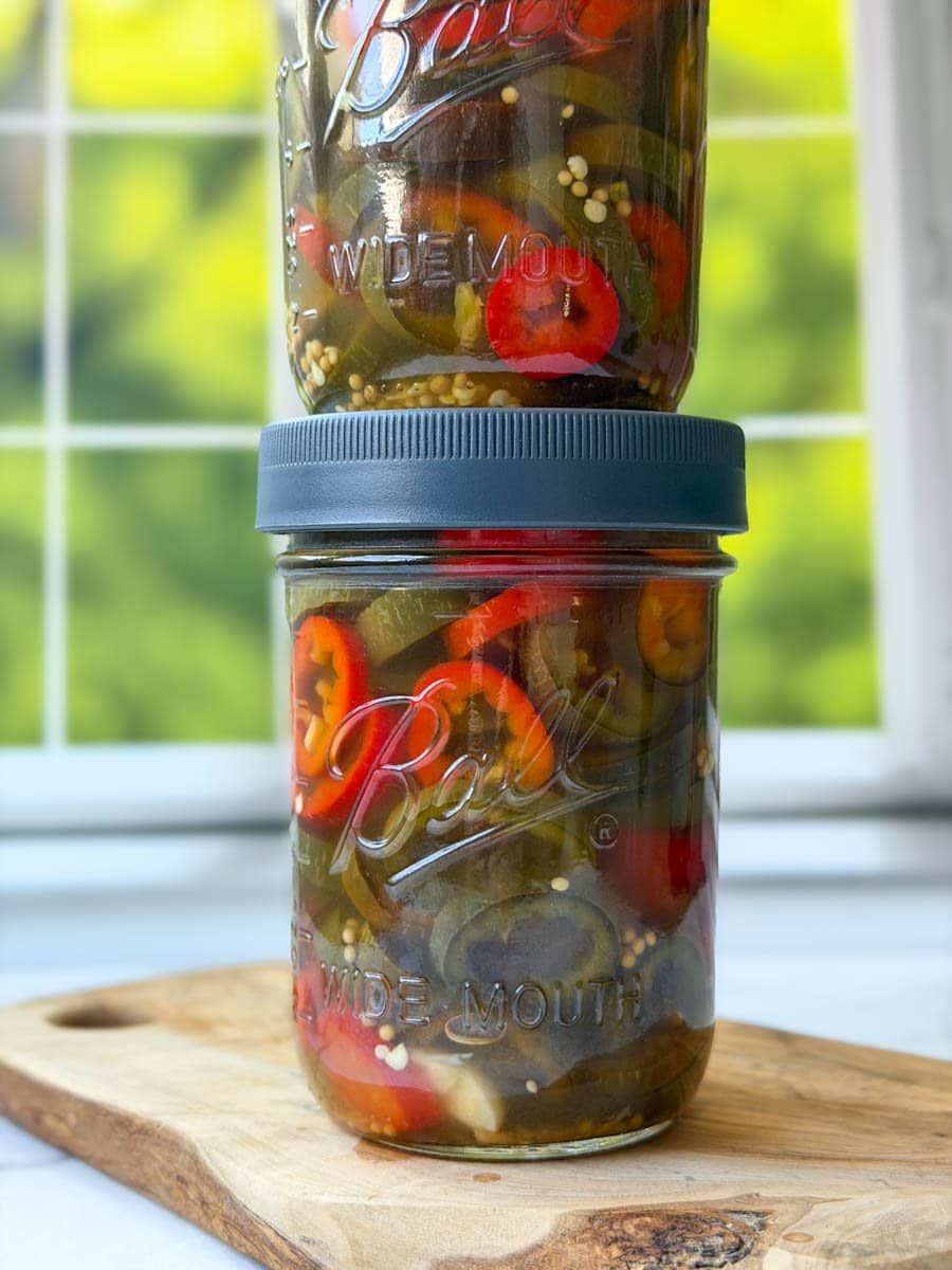 Two pint jars are stacked on top of each other full of sliced pickled jalapeños.